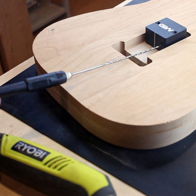 bottom of a guitar getting repaired with a jig and drill 